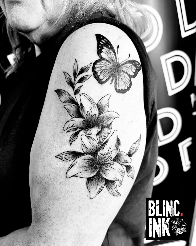 Lily & Butterfly: a custom engraving-style tattoo on the upper arm by Clive Camilleri at Dermoda Studio, Highbridge, Somerset.